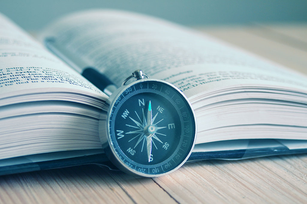 An old analog compass pointing North North East leaning on the edge of an open book.