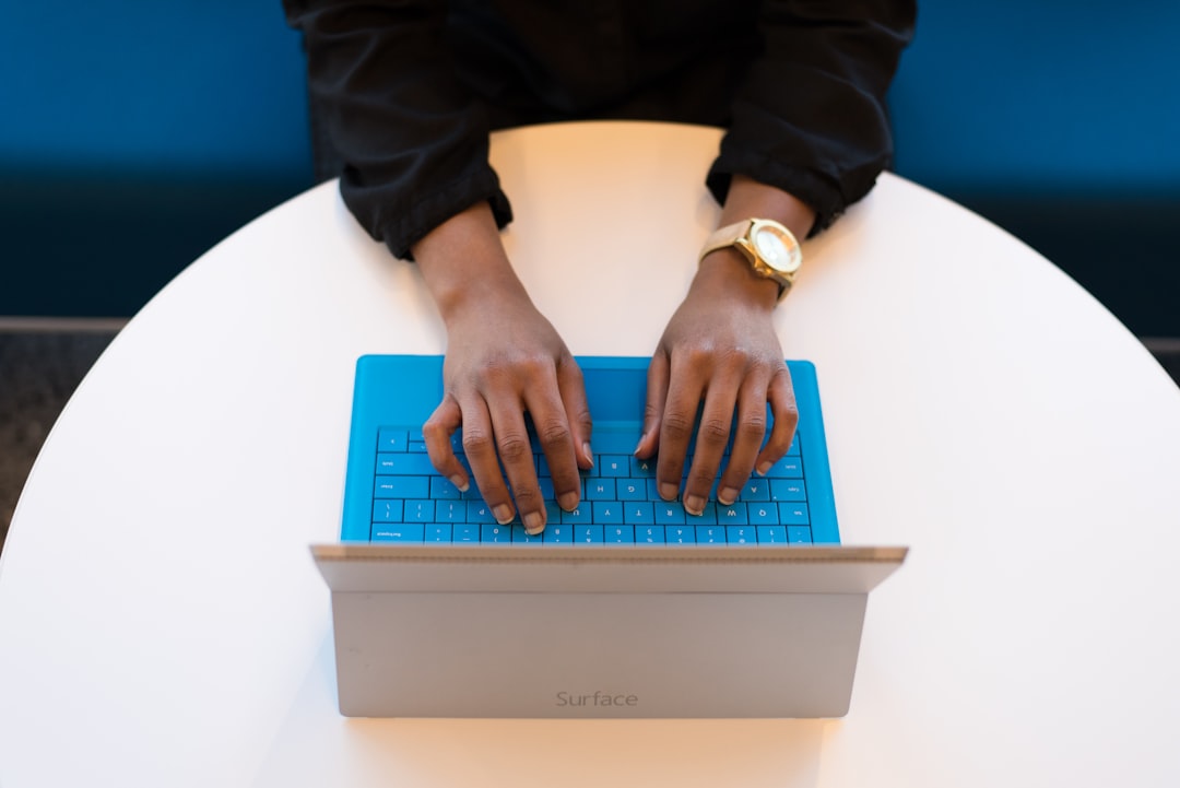 Hands of a woman of color typing on a blue keyboard of a Microsoft Surface tablet.